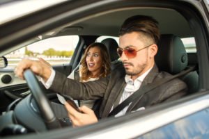 A concerned woman in a car with a man who is texting while driving.