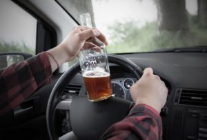 A man drives while holding alcohol on the steering wheel