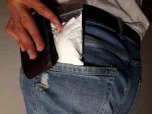 A man putting drugs and his wallet in his pants pocket.