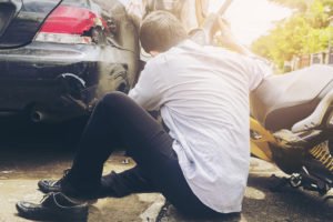 A motorcyclist sits next to a car after a crash