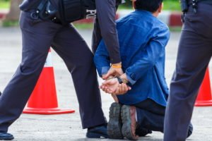 Police officers arrest a kneeling man.