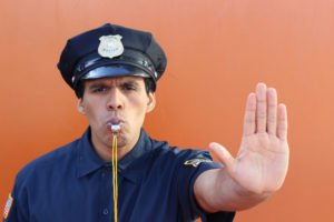 A police officer blowing a whistle while holding up his hand.