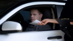 A police officer hands over a ticket to an upset driver.