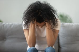 A sad woman on a couch, holding her head.
