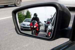A side-view mirror view of a motorcyclist riding between traffic.