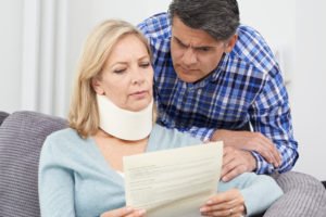 A woman in a neck brace looks at a bill with her husband