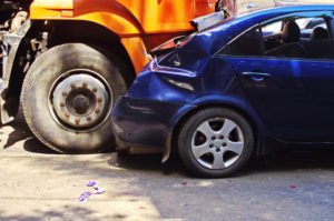 A blue car, crushed by an orange truck