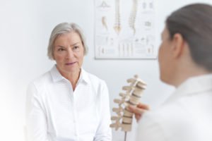 A doctor shows a model spine to an older woman.
