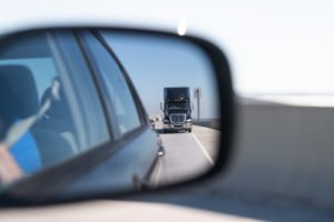 A rear-view mirror view of a semi-truck approaching a car.