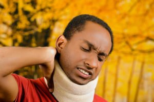A man in a neck brace, holding his neck.