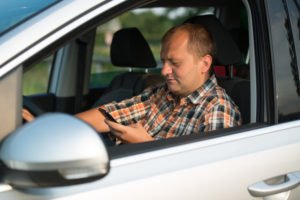 A man in a plaid shirt texting while driving.