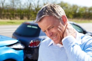 An older man rubbing his neck after a car accident.