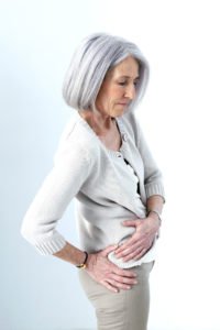 An older woman holds her hip in pain.