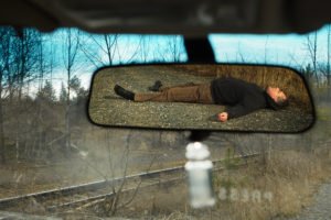 View from a rear-view mirror of an injured man laying on the road.