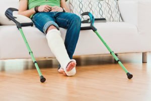 A woman in a leg brace uses crutches during physical therapy.