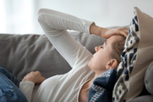 A woman laying on her couch, holding her head in pain.