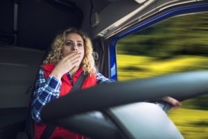 A woman yawns while driving a truck.
