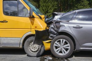 A crash between a yellow delivery van and a gray car.