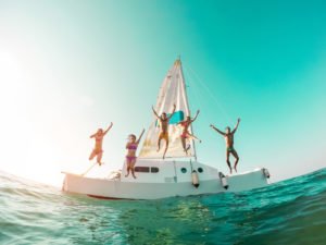 group of friends jumping off a sailboat into the water
