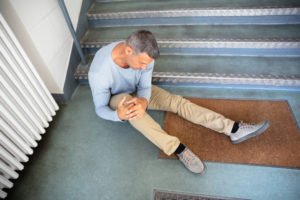 A man sitting on the floor, holding his knee, after falling down stairs.