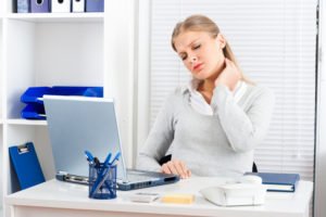 A woman sitting in front of a laptop holding her neck in pain.