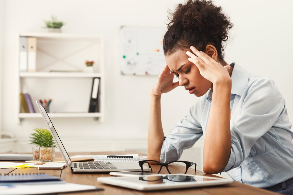 black woman with a headache at her desk