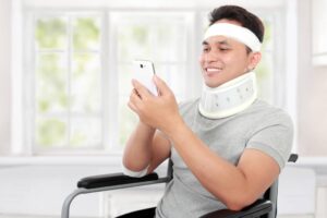 A man in a wheelchair and a neck brace uses his phone.